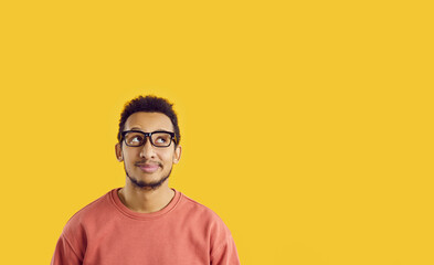 Smiling dreamy african american guy imagines something nice on bright yellow banner background....