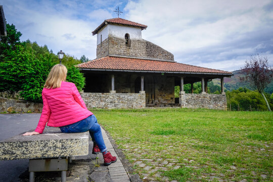 Young woman with a fuchsia coat contemplating the Romanesque hermitage of San Pelayo in the Basque Country