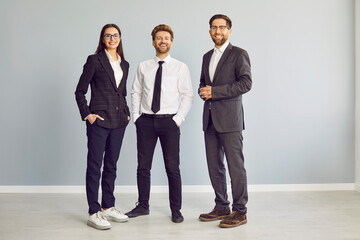 Full length portrait of a group of three young cheerful business people in suits standing...