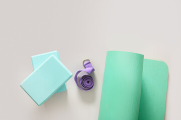 Green mat, yoga blocks and violet belt on gray background. Top view. Yoga practice, stretching concept.