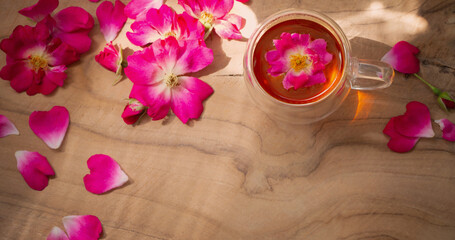 Fototapeta na wymiar pink rose petals and cup of tea on wooden background