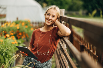 Front view of a pretty blond woman holding a tablet in the garden.
