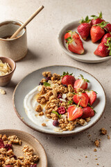 Healthy breakfast: fresh granola, muesli with yogurt, strawberry and honey on beige textured background