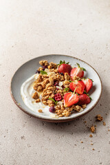 Healthy breakfast: fresh granola, muesli with yogurt, strawberry and honey on beige textured background. Text space