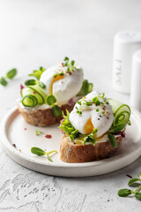Poached egg sandwich with cucumber and microgreens. Healty breakfast bruschetta on light background. Keto diet, text space