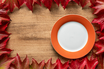 Thanksgiving day concept with empty plate on wooden table with autumn leaves, Thanksgiving and harvest day
