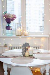 Christmas table setting with burning candles, retro lights and champagne glasses. Warm and cozy atmosphere