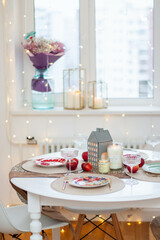 Christmas table setting with burning candles, retro lights and champagne glasses. Warm and cozy atmosphere