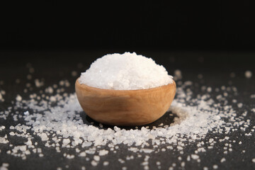 salt into a wooden spoon from a bowl on a black background. Coarse sea salt.