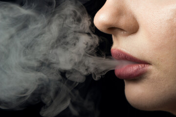 Tobacco smoke comes out of women's lips on a black background