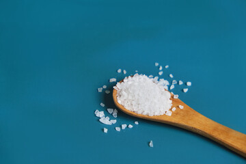 Coarse salt crystals on a blue table. Wooden spoon with sea salt. Background for advertising salty.