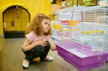 Little girl child sitting nearby cage for rodent at pet shop