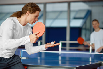 Man and woman playing table tennis, focus on sportsman player serving