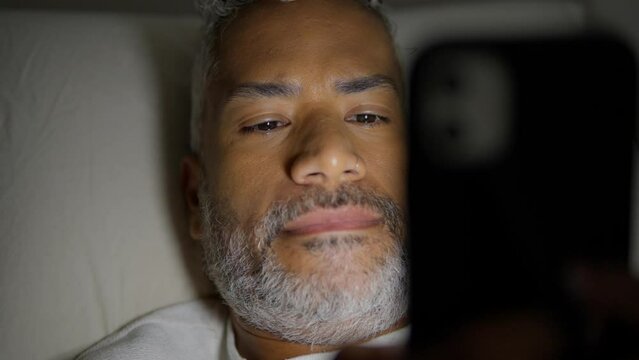 Insomnia and anxiety concept at night. Close up of black man divided between slepping or sing social media on mobile phone.