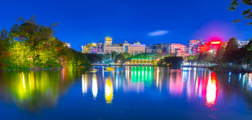 Fototapeta na wymiar Hanoi City Old Quarters Lake at night glowing with vibrant colourful city lights surrounded by old historic buildings small bridge crossing the lake into a temple on a small island Hanoi Vietnam