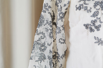 The sleeve of a button-up lacy blouse. Gray floral pattern on a white shirt. 