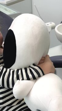 a little girl in a striped blouse in a dental office with a soft toy A sleepwalker or white astronaut laughs hugging waiting 