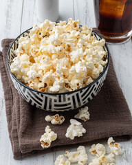 Popcorns on a bowl with salt over and soda wooden table