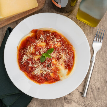 Raviolonis or raviolis with tomato sauce over wooden table