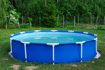 Blue portable country pool on the lawn of a country garden.