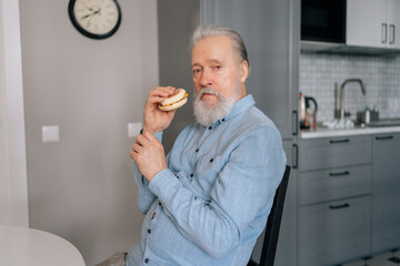 Portrait of handsome bearded mature elderly male eating unhealthy fast food enjoying dinner at home...