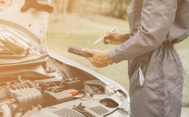Obraz premium Young mechanic opens the bonnet to inspect the engine for damage and does professional maintenance. He puts on his uniform and inspects.