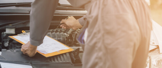 A car mechanic checks and maintains the engine for the customer. The car hood and master inspector...
