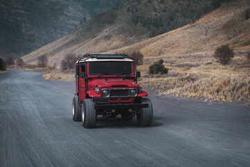 Plakat Close up shot of driving red jeep on Bromo road. Rental off road vehicle for exploring mountain volcano reservation