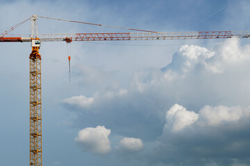 Tall metal crane on sky with cumulus clouds background