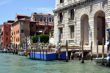 A row of different houses on the waterfront with a pier and boats in Venice, Italy. View against the background of the blue sky