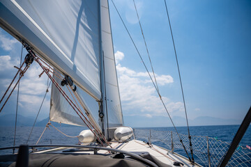 Fototapeta na wymiar Yacht sailing in an open sea. Close-up view of the deck, mast and sails. Clear sky, waves and water splashes