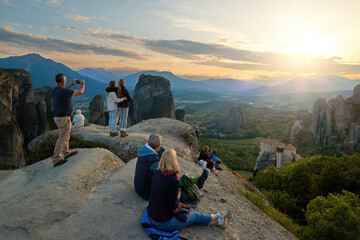 Travel Concept: View from behind at a group of tourists, standing  on a cliff, watching the sunset over the valley with the Meteora monasteries complex. Greece Unesco site.