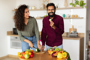 Happy young arab couple cooking healthy meal together in kitchen interior and laughing, man eating...