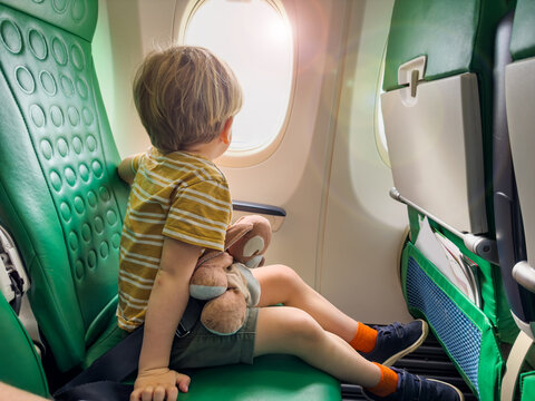 Little boy sit near window in the plane looking at porthole