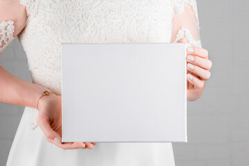 Bride holding white canvas mockup on white wall background. Minimal stile blank mockup, picture...