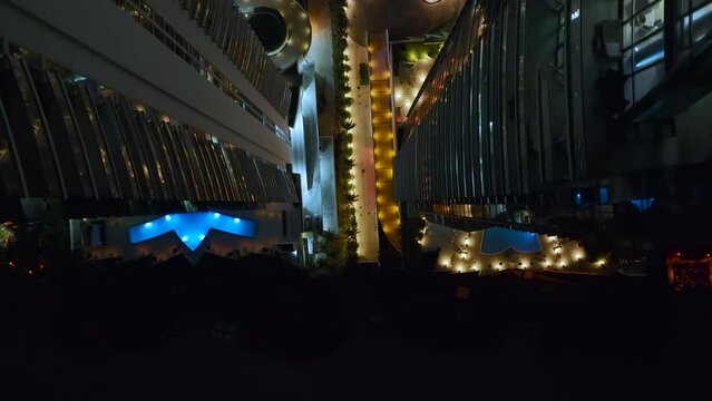 View from above of brightly illuminated high skyscraper hotel with swimming pool recreational area in downtown of Sunny Isles Beach city in Florida, USA. American tourist urban district at night