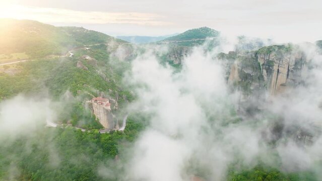 Aerial view of a valey Meteora with clifs covered by mist.  Epic view of Holy Monastery of Rousanos - Saint Barbara complex on the top of meteora cliff among clouds and mist. A UNESCO World Heritage S
