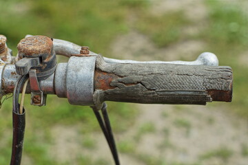 very old cracked rubber throttle stick with a metal lever and part of the steering wheel of a retro non-working motorcycle outdoors during the day