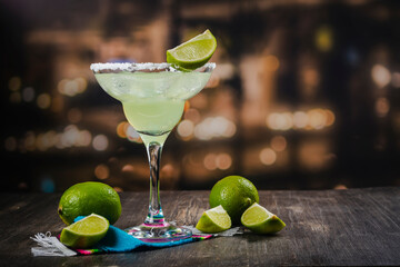 Margarita cocktail with sliced and whole limes on wooden bar table. Mexican party background