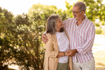 Smiling old european husband hugging wife enjoy walk together, active lifestyle in park, romantic date