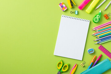 Back to school concept. Empty notepad with school stationery on green background.