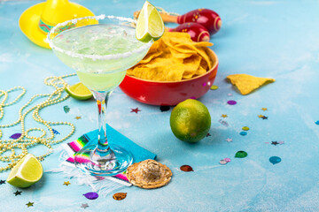 Margarita cocktail with sliced and whole limes, nachos and salt on blue stone table. Mexican party background