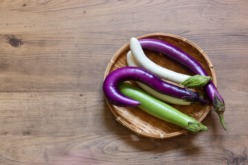 木材背景の様々な色の笊にのせた細長い茄