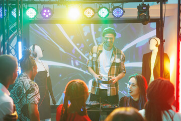 People dancing and enjoying dj show at disco party in nightclub. Young man musician performing and...