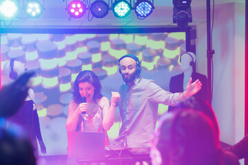 Musicians on stage engaging people to party while performing at nightclub concert. Dj and singer speaking in microphone and entertaining crowd dancing on dancefloor in club
