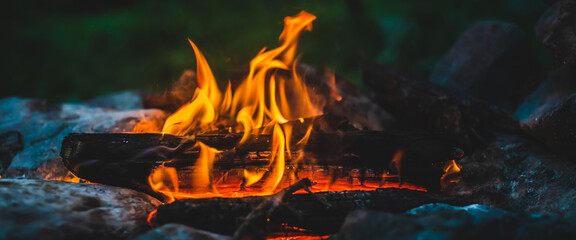 Vivid smoldered firewoods burned in fire close-up. Atmospheric warm background with orange flame of...
