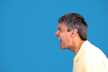 Side view of mature man shouting looking aside, blue background