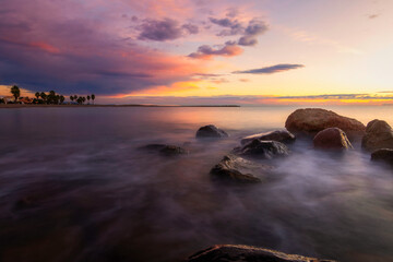 amanecer con nubes de colores en la playa con rocas