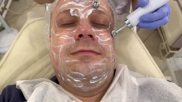 A cosmetologist performs a microcurrent procedure on the patient's face. Hardware cosmetology in the salon of the clinic for the client. A man is lying down for a facial microcurrent procedure to stim