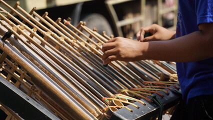 A man is playing angklung. That is a multitonal musical instrument that developed from the Sundanese people. Angklung is made of bamboo